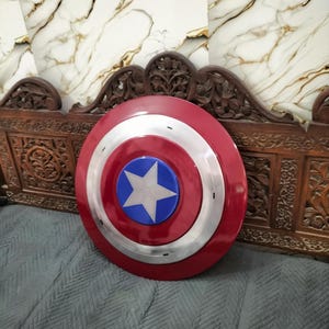 Op de afbeelding: Een rood, wit en blauw schild met een sterembleem. Het schild heeft een cirkelvormig ontwerp met een zilveren band die de rode buitenring van het blauwe midden scheidt. De ster is wit en is gecentreerd op de blauwe cirkel.
