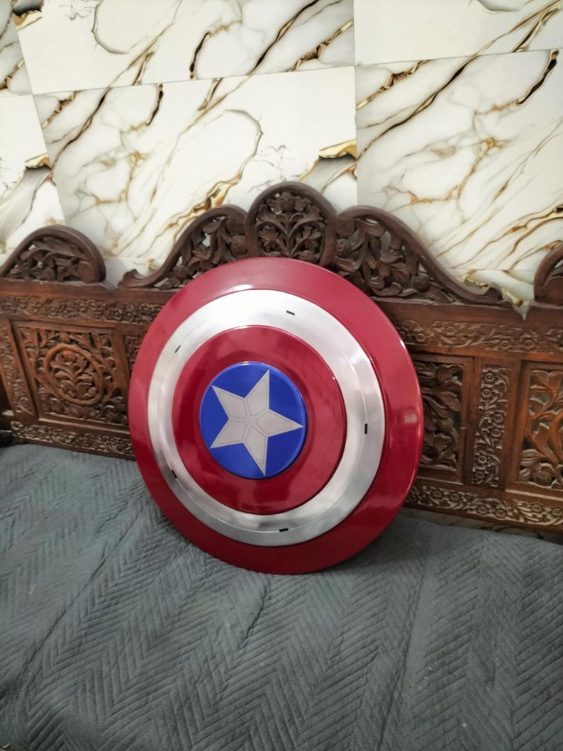 Op de afbeelding: Een rood, wit en blauw schild met een sterembleem. Het schild heeft een cirkelvormig ontwerp met een zilveren band die de rode buitenring van het blauwe midden scheidt. De ster is wit en is gecentreerd op de blauwe cirkel.