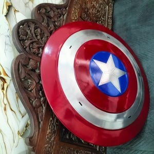 Op de afbeelding: Een rood, wit en blauw Captain America schild. Het schild heeft een rode buitenring, een zilveren binnenring en een blauw midden met een witte ster. Een replica van het iconische schild uit de strips.