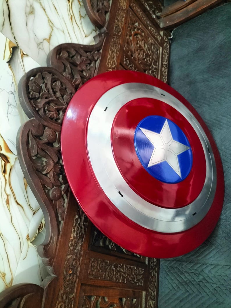 Op de afbeelding: Een rood, wit en blauw Captain America schild. Het schild heeft een rode buitenring, een zilveren binnenring en een blauw midden met een witte ster. Een replica van het iconische schild uit de strips.