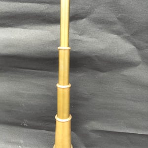 May include: A brass telescope with a cylindrical design. The telescope has multiple sections, with a flared base and a narrower top. The brass has a warm, golden hue, and the telescope appears to be a vintage or antique item.