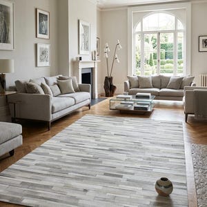 Könnte beinhalten: Ein rechteckiger Teppich mit einem horizontalen Patchwork-Muster aus Kuhfellstreifen in verschiedenen Grau-, Weiß- und Cremetönen. Der Teppich hat eine kurzflorige Textur und liegt auf einem Holzboden mit Fischgrätenmuster.