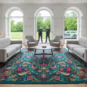 May include: A teal area rug with a detailed floral and bird pattern dominates the room. Two gray sofas and two armchairs frame a round coffee table. The room has large windows and doors, with a view of the outside.