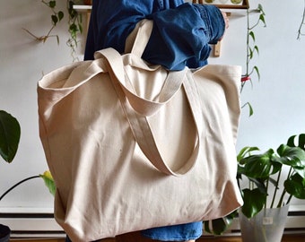 May include: A large, off-white canvas tote bag with thick, sturdy straps. The bag is empty and has a slightly textured surface.