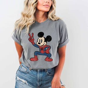 A woman wearing a gray t-shirt with a cartoon character of Mickey Mouse and Spider-Man printed on it.