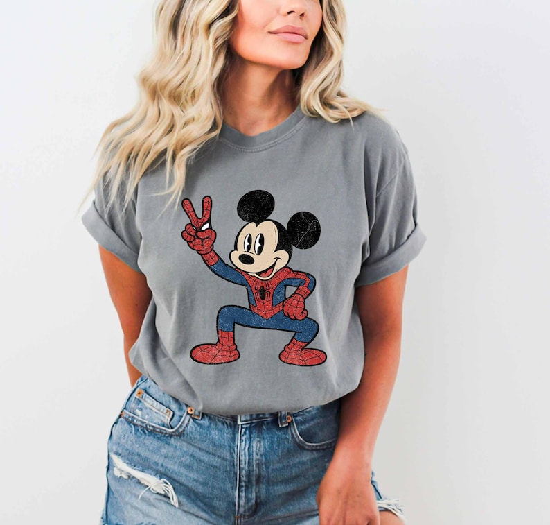 A woman wearing a gray t-shirt with a cartoon character of Mickey Mouse and Spider-Man printed on it.