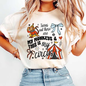 A woman wearing a white t-shirt with a graphic design featuring a monkey, circus, and text.