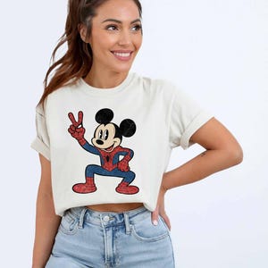 A woman wearing a white t-shirt with a cartoon character of Mickey Mouse and blue jeans, smiling and posing for the camera.