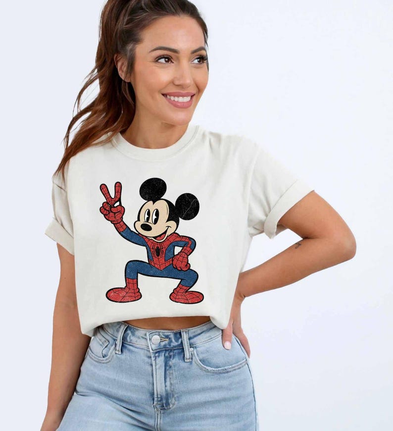 A woman wearing a white t-shirt with a cartoon character of Mickey Mouse and blue jeans, smiling and posing for the camera.