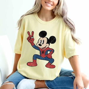 A woman wearing a yellow t-shirt with a cartoon character of Mickey Mouse and Spider-Man printed on it.