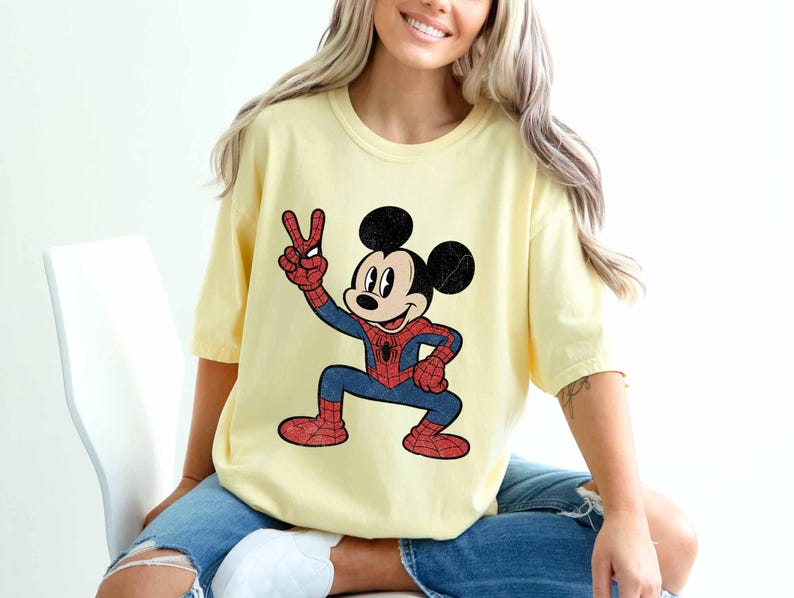 A woman wearing a yellow t-shirt with a cartoon character of Mickey Mouse and Spider-Man printed on it.