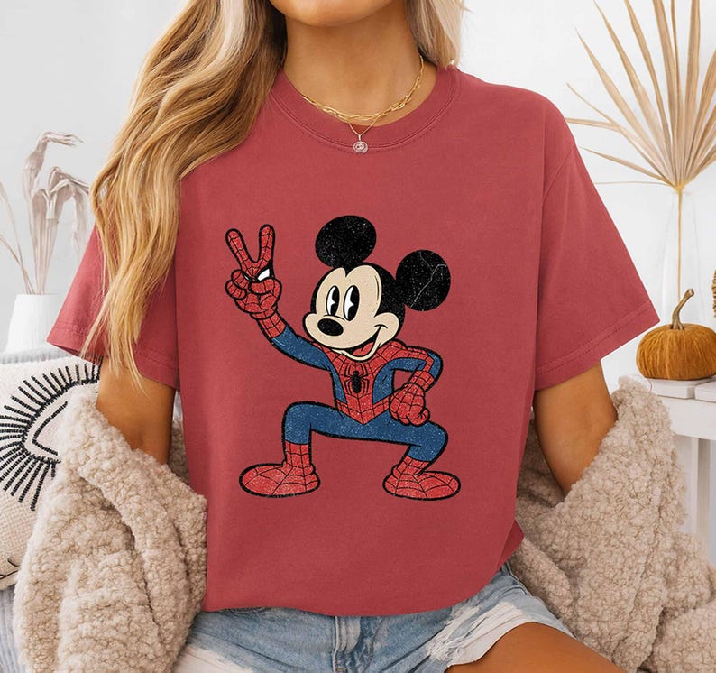 A woman wearing a red t-shirt with a cartoon character of Mickey Mouse and Spider-Man printed on it.