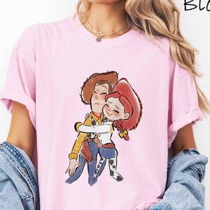 A woman wearing a pink t-shirt with a cartoon character from the Toy Story movie hugging another character.