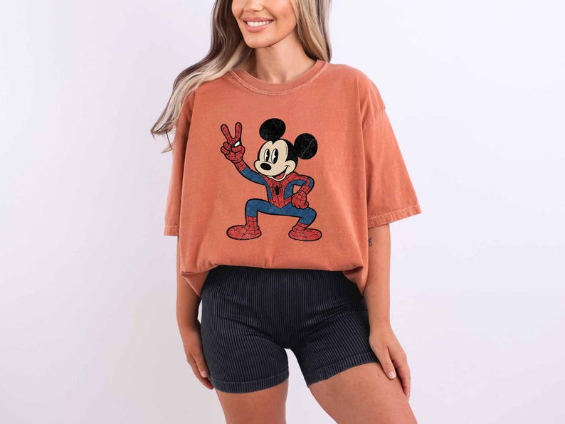 A woman wearing a red t-shirt with a cartoon character and black shorts is smiling.