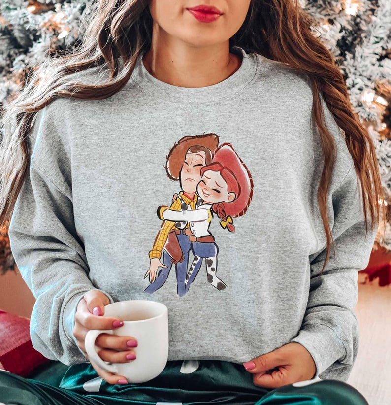 A woman wearing a gray sweatshirt with a cartoon character printed on it, holding a white mug in her hand.