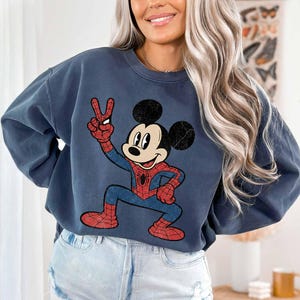 A woman wearing a blue sweatshirt with a cartoon character of Mickey Mouse on it, smiling and posing for the camera.