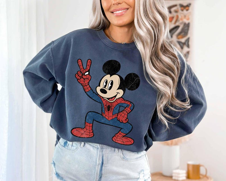 A woman wearing a blue sweatshirt with a cartoon character of Mickey Mouse on it, smiling and posing for the camera.