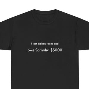 Può includere: T-shirt nero con testo bianco: "Ho appena fatto le tasse e devo $5000 alla Somalia". La maglietta è a girocollo. Il testo è centrato sul davanti della maglietta.