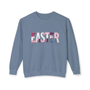 Może przedstawiać: Błękitna bluza z napisem "EASTER" na piersi. Litery wykonane są z patchworkowej tkaniny w odcieniach różu, bieli i błękitu. Bluza ma długie rękawy i okrągły dekolt.