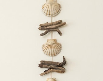 May include: A vertical wall hanging decoration featuring three off-white fan-shaped seashells alternating with two clusters of brown driftwood pieces, all strung together on a thin natural twine cord with a small loop at the top.
