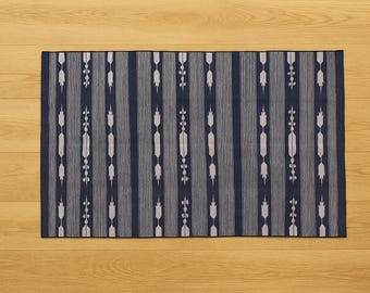 Pode incluir: Tapete retangular com padrão azul marinho e branco. O tapete apresenta listras verticais com um design floral repetitivo. O tapete é colocado sobre uma superfície de madeira castanha clara.