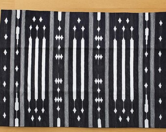 Könnte beinhalten: Schwarz-weiß gemusterter Stoff. Das Design zeigt vertikale Streifen und geometrische Formen. Der Stoff ist rechteckig und scheint aus gewebtem Material zu bestehen. Das Farbschema ist ein starker Kontrast aus Schwarz und Weiß.