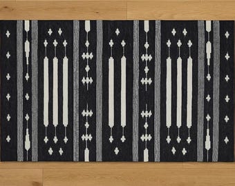 May include: A rectangular black and white patterned rug. The rug features vertical white stripes and decorative elements against a black background. The design includes various shapes and patterns, creating a visually appealing textile.