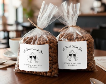 May include: Two clear cellophane bags filled with brown treats, tied with twine. Each bag has a white label with the text "A Sweet Thank You" and the names "STEVEN & MELISSA" with the date "9.30.2026" below. The labels feature a graphic of two toasting glasses.