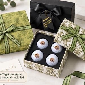May include: A set of four white golf balls featuring a golden retriever illustration, presented in a decorative gift box with a green ribbon printed with the words BEST WISHES. The set includes a black gift box with a bow and a tag reading bestlove.