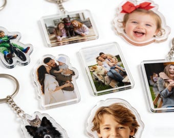May include: A collection of clear acrylic keychains featuring personalized photos. The keychains showcase various family portraits, including images of children, adults, and pets. Each keychain has a silver metal ring.