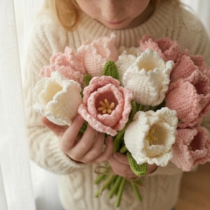 May include: A bouquet of crocheted tulips in shades of white and pink, with green leaves. The handmade flowers are held together, showcasing the intricate stitchwork and soft color palette. The bouquet is a charming, handcrafted item.