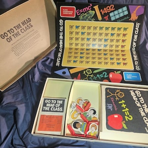 May include: An open vintage board game box with the title "GO TO THE HEAD OF THE CLASS" printed on the box and game pieces. The game includes cards, game pieces, and a game board with math symbols and equations.