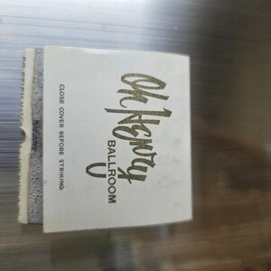 May include: A vintage matchbook with the words "Oh Henry Ballroom" in gold lettering. The matchbook is white with a gray edge and the text "Close cover before striking".