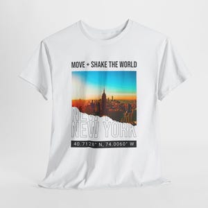Può includere: T-shirt bianco con grafica dello skyline di New York City al tramonto. La maglietta presenta la scritta "MOVE + SHAKE THE WORLD" sopra l'immagine e "NEW YORK" sotto. Le coordinate 40.7128° N, 74.0060° W sono stampate in basso.