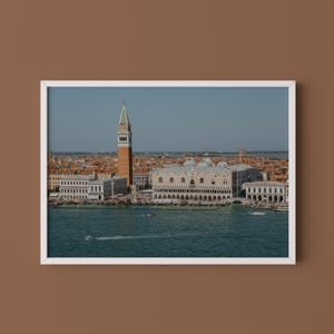 May include: A framed landscape photograph of the Venice waterfront featuring the Doge's Palace and St. Mark's Campanile. The scene shows historic buildings with terracotta roofs, a tall bell tower, and a blue canal with small boats in the foreground.