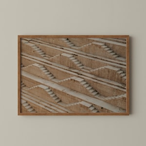 May include: A framed print featuring a detailed architectural design of a stepwell. The image showcases a series of descending staircases and platforms, creating a geometric pattern in shades of beige and gray. The print is encased in a wooden frame.