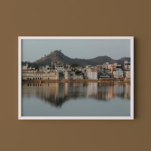 May include: A framed photograph of a scenic landscape featuring a body of water reflecting a city skyline. The buildings are primarily white and beige, with a mountain range in the background. The sky is a soft gray.