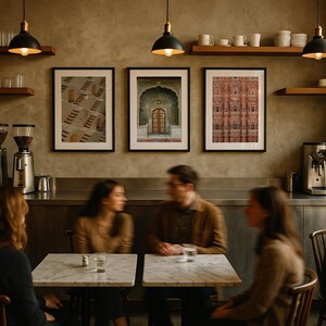 Op de afbeelding: Een koffiebar-interieur met drie ingelijste architecturale prints aan een getextureerde muur, houten planken met witte keramische mokken, zwarte hanglampen, roestvrijstalen espressomachines en tafels met marmeren bladen en houten stoelen.
