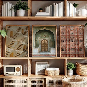 Op de afbeelding: Drie ingelijste wandkunstwerken op een houten plank. De linker print toont een beige stenen trap, de middelste print een groene boogdeur en de rechter print een rood gebouw met een gevel vol boogramen.