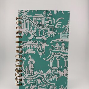 May include: A teal blue spiral bound notebook with a white and teal patterned design featuring pagodas and stylized floral motifs.