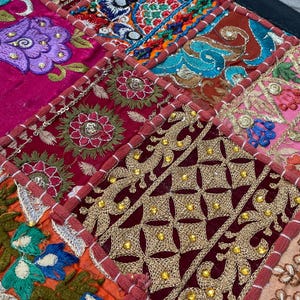 May include: A patchwork textile featuring a vibrant mix of colors and patterns. The design includes squares of deep red, fuchsia, and gold, adorned with intricate embroidery and beadwork. Floral and geometric motifs are prominent.