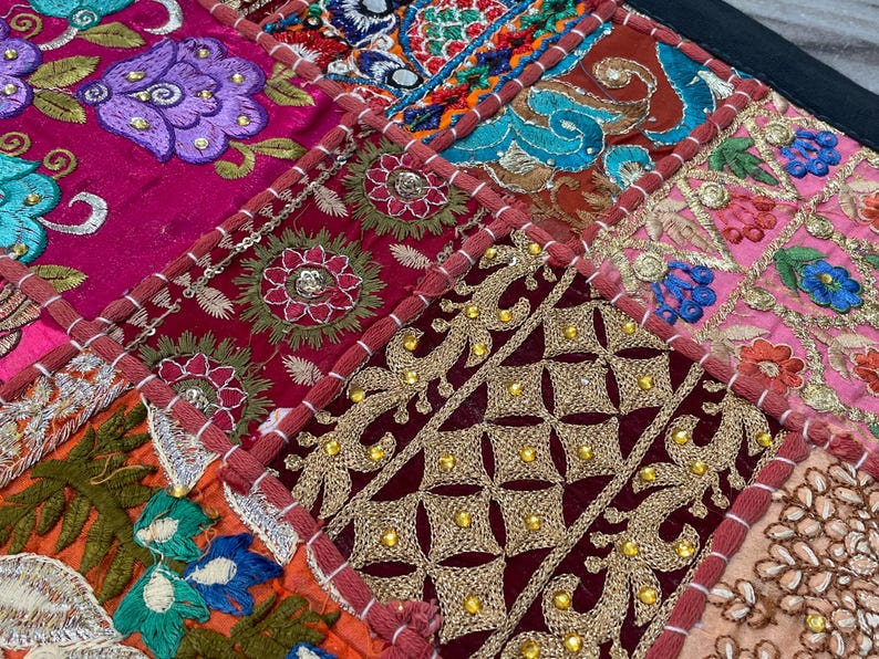 May include: A patchwork textile featuring a vibrant mix of colors and patterns. The design includes squares of deep red, fuchsia, and gold, adorned with intricate embroidery and beadwork. Floral and geometric motifs are prominent.