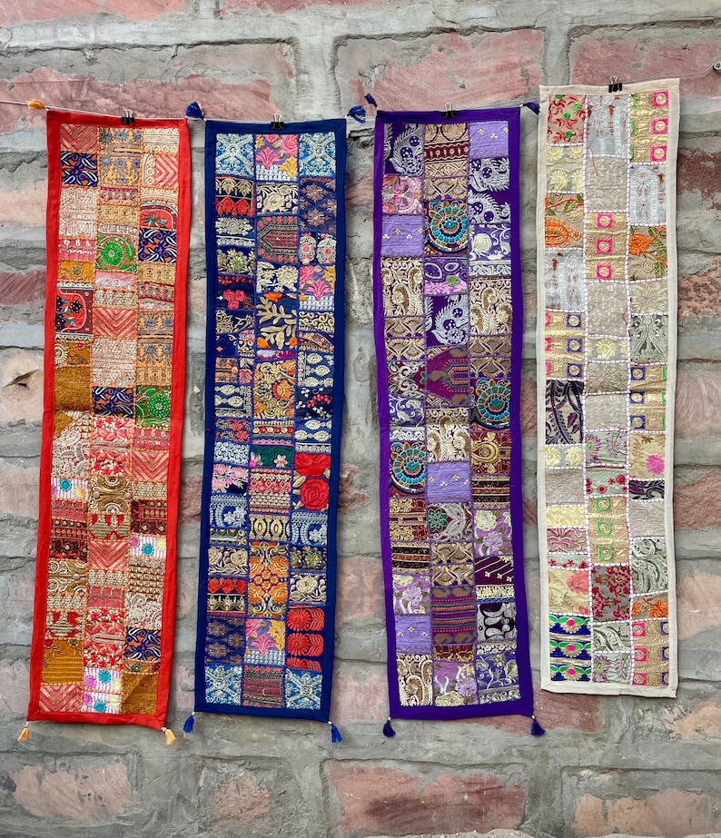 May include: Four colorful, rectangular wall hangings with patchwork designs. The hangings feature red, blue, purple, and cream borders, with intricate patterns and tassels. Each piece is unique, showcasing a variety of colors and textures.