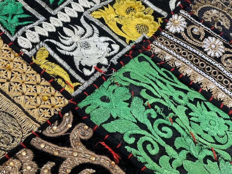May include: Close-up of a patchwork textile with intricate embroidery. The design features various geometric and floral patterns in gold, green, white, and black. The patches are sewn together with red thread, creating a vibrant and detailed texture.