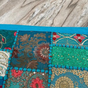 May include: A patchwork textile with a vibrant mix of colors and patterns. The design features squares of teal, turquoise, and gold fabric with floral and paisley embroidery. A bright blue border and tassels complete the look.