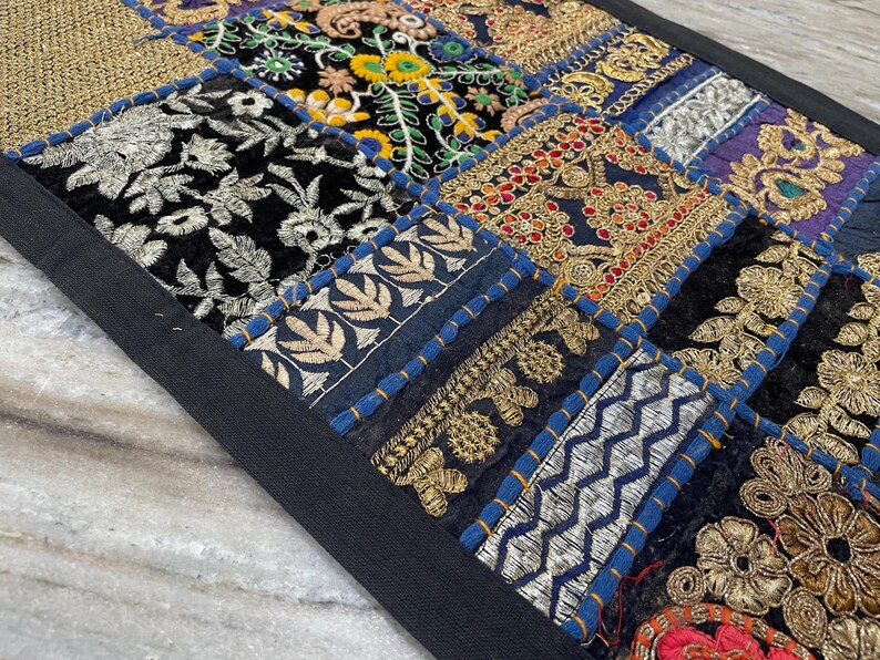 May include: A patchwork textile with a black border. The design features squares of various fabrics, including black velvet with silver embroidery, gold brocade, and floral patterns. The colors include gold, blue, black, and red.