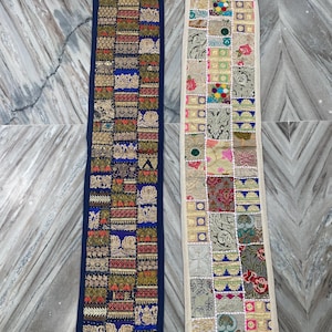 May include: Two rectangular, decorative textile runners. One is navy blue with a patchwork design of gold, red, and green embroidered squares. The other is cream-colored with a similar patchwork design featuring various colors and patterns.