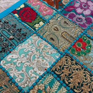 May include: A patchwork textile with a vibrant mix of colors and patterns. The design features squares of embroidered fabric in teal, turquoise, gold, and magenta. Each square has a unique floral or paisley design, with a teal border.