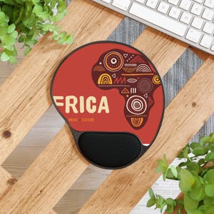 Puede incluir: Alfombrilla de ratón ergonómica roja y negra con un diseño del continente africano. El diseño incluye formas geométricas en amarillo, naranja y marrón. La palabra "FRICA" está impresa en beige, con "MUSIC | CULTURE" debajo.