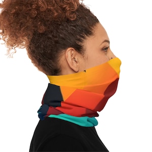 Könnte beinhalten: Ein farbenfrohes Halstuch mit geometrischem Design. Der Gesichtsschutz zeigt ein Muster aus orangefarbenen, roten, gelben, türkisfarbenen und marineblauen Formen. Das Accessoire wird um den Hals getragen und bedeckt das untere Gesicht.